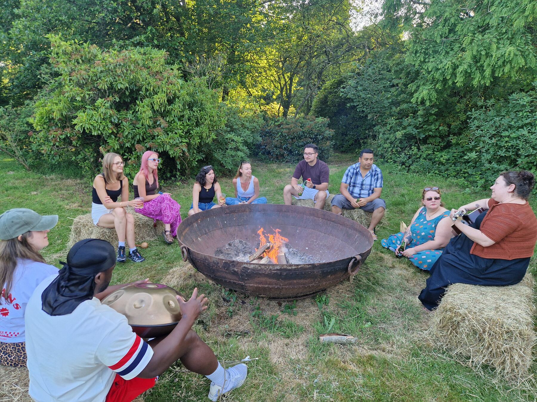 People sitting close around the fire, one playing a drum