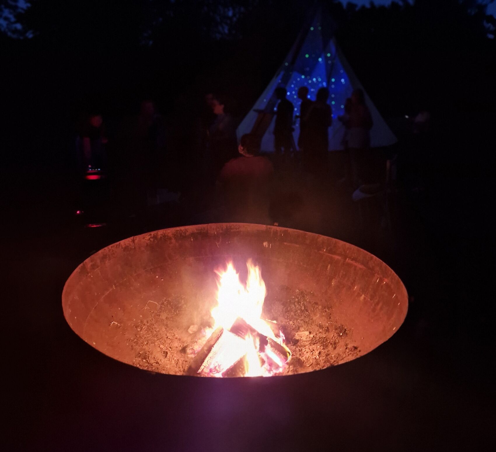 The fire bowl at night with the blue-lit tipi behind