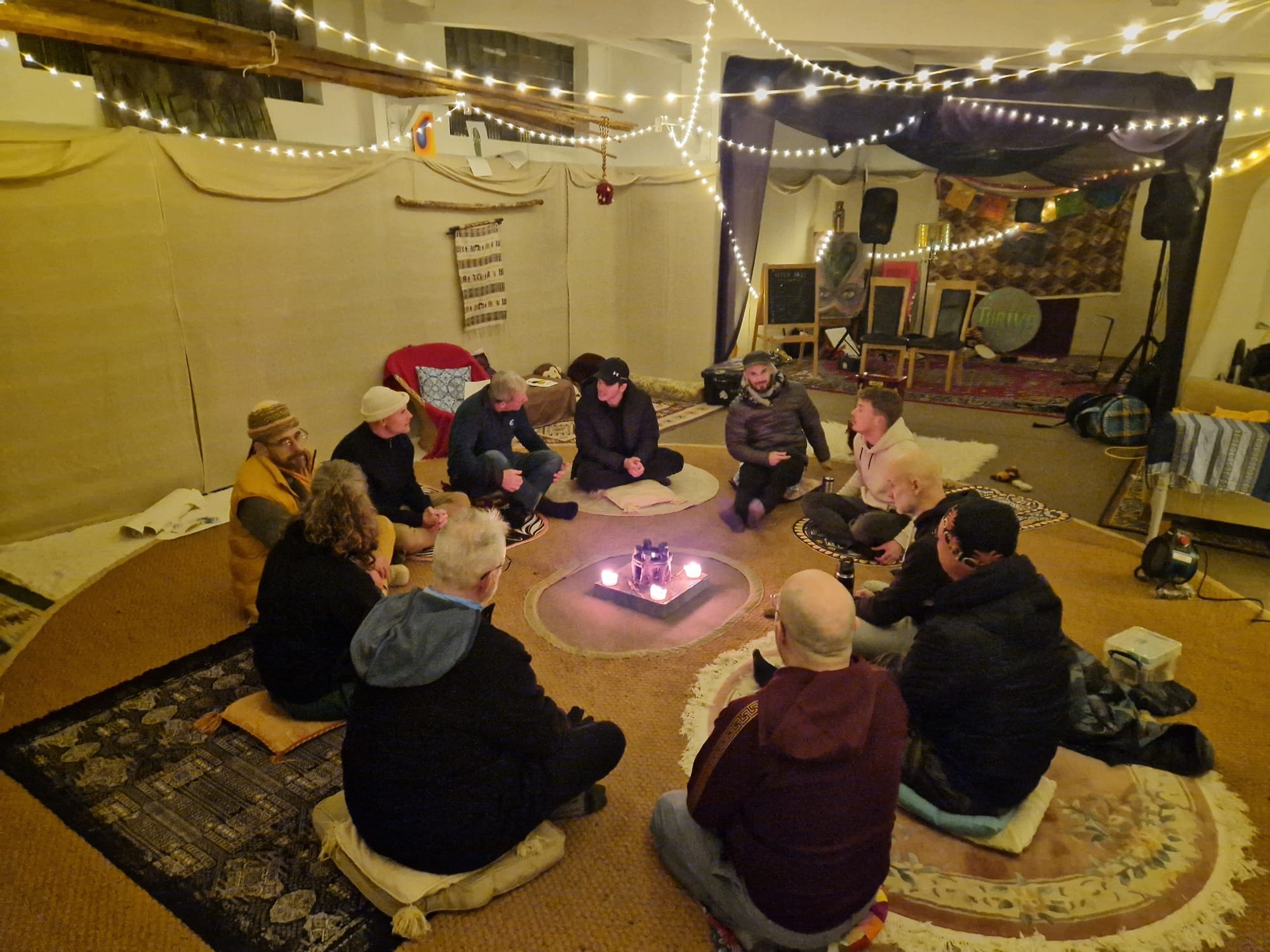 The circle in the hall under fairy lights, candles at the centre