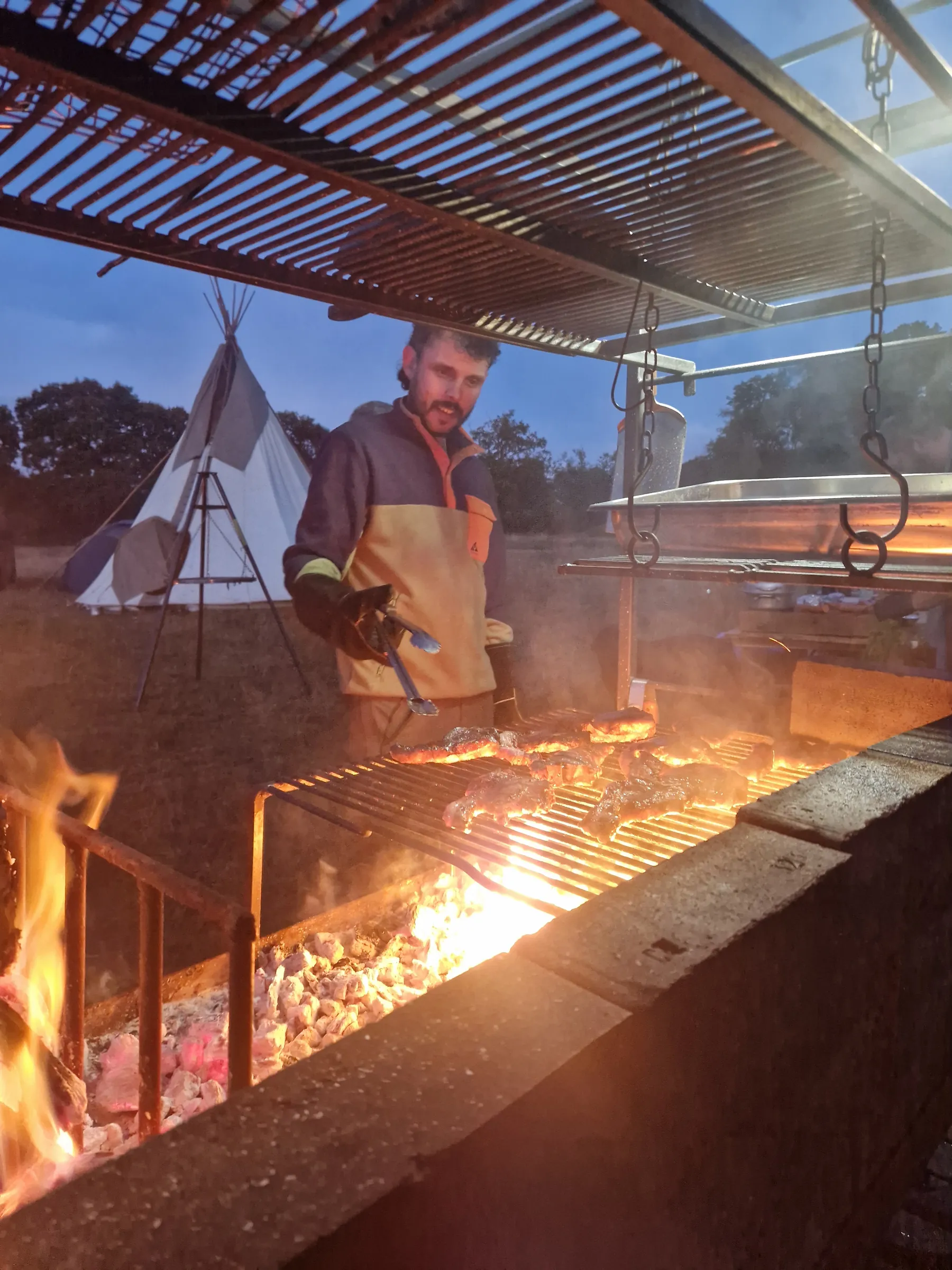 Meat cooking over an open fire grill at dusk