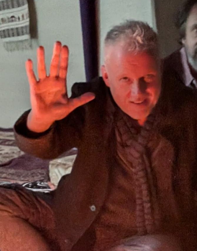Sean Crooks, by candlelight, hand raised in greeting